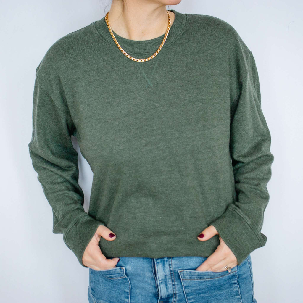 Person wearing a green Excel Therapy Services sweatshirt and blue jeans with a gold chain necklace against a white background